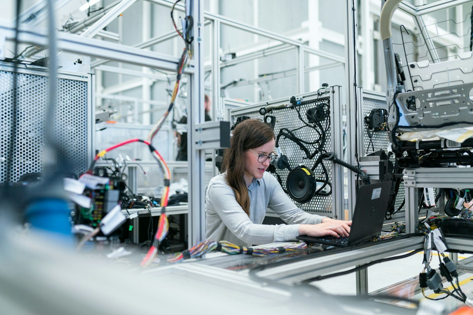 Engineer at a laptop in an industrial manufacturing facility surrounded by wiring and equipment