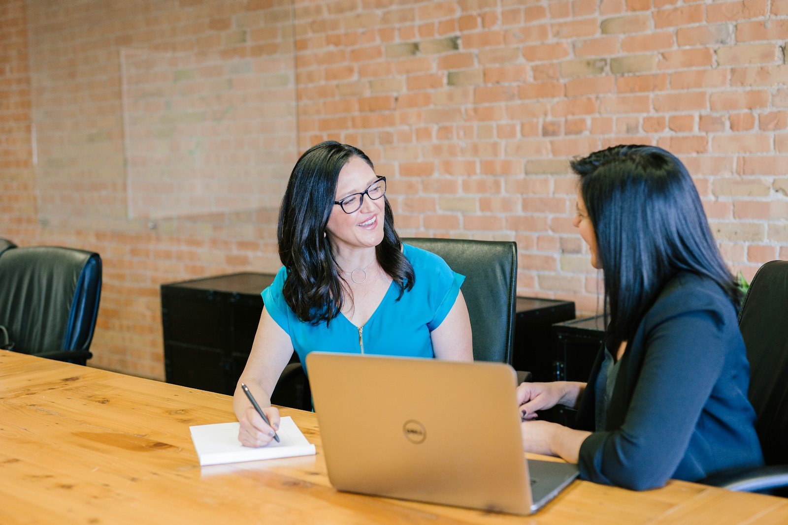 Two professionals in a consulting discussion at a boardroom table with laptops